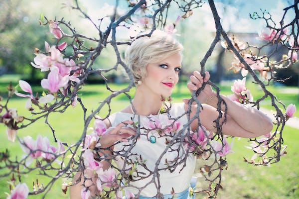 A blonde girl peeps between the branches of a magnolia tree